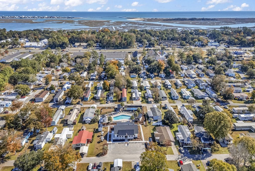 A wide aerial view of a residential community near a coastal marshland with neatly arranged mobile homes and a visible central pool are in murrells inlet sc